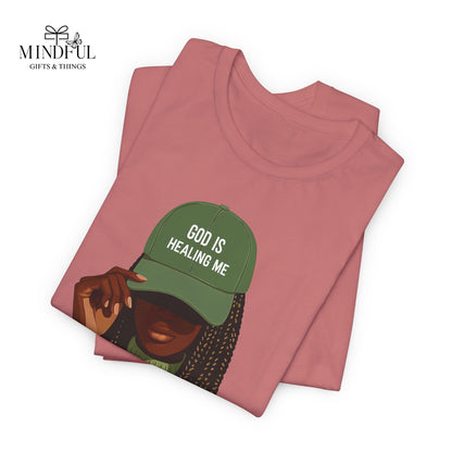 God Is Healing Me Tee — Inspirational Faith T‑Shirt with Green Cap Graphic
