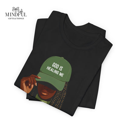 God Is Healing Me Tee — Inspirational Faith T‑Shirt with Green Cap Graphic